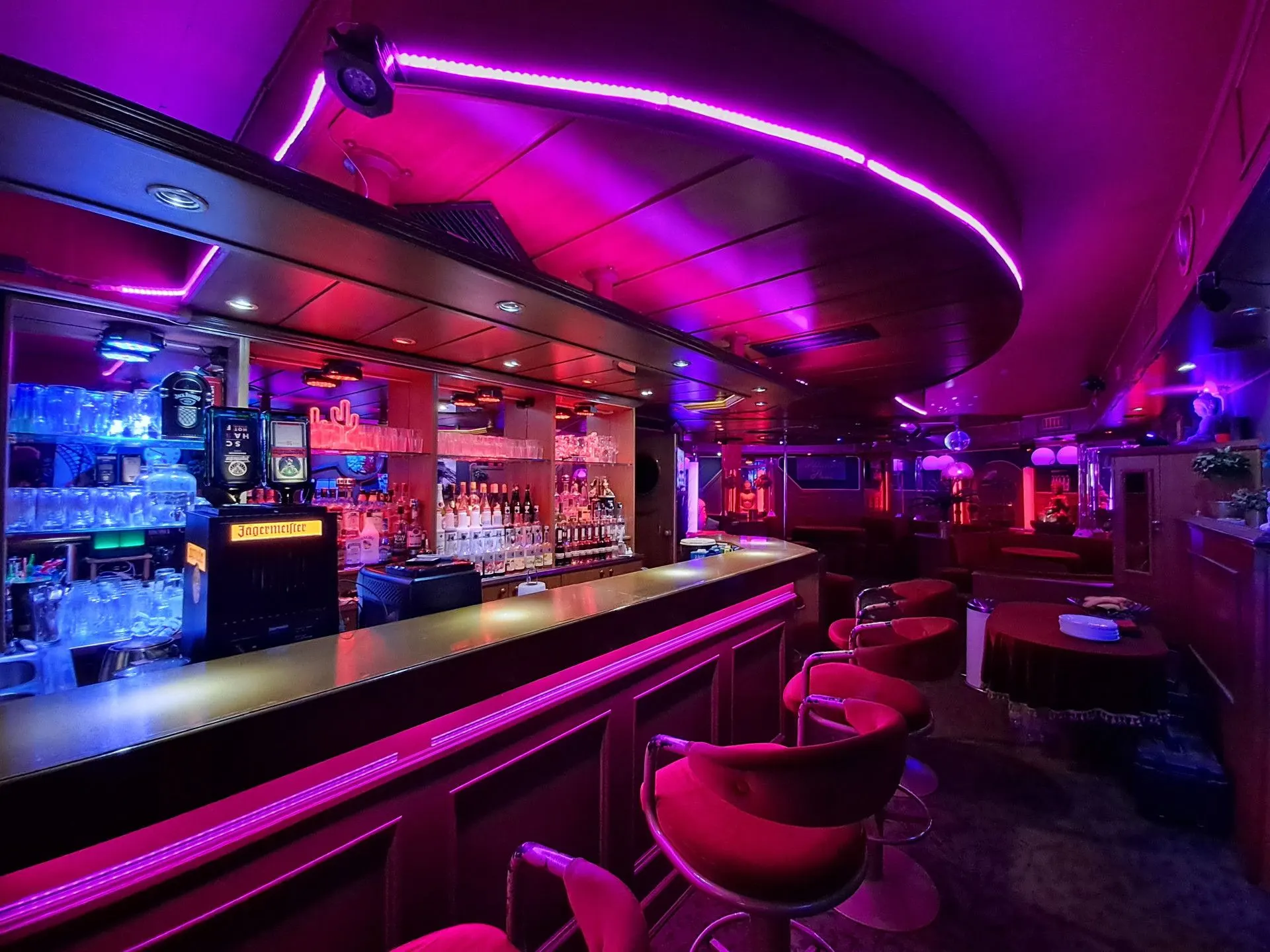 Long bar counter with red stools and a magenta light strip on the ceiling