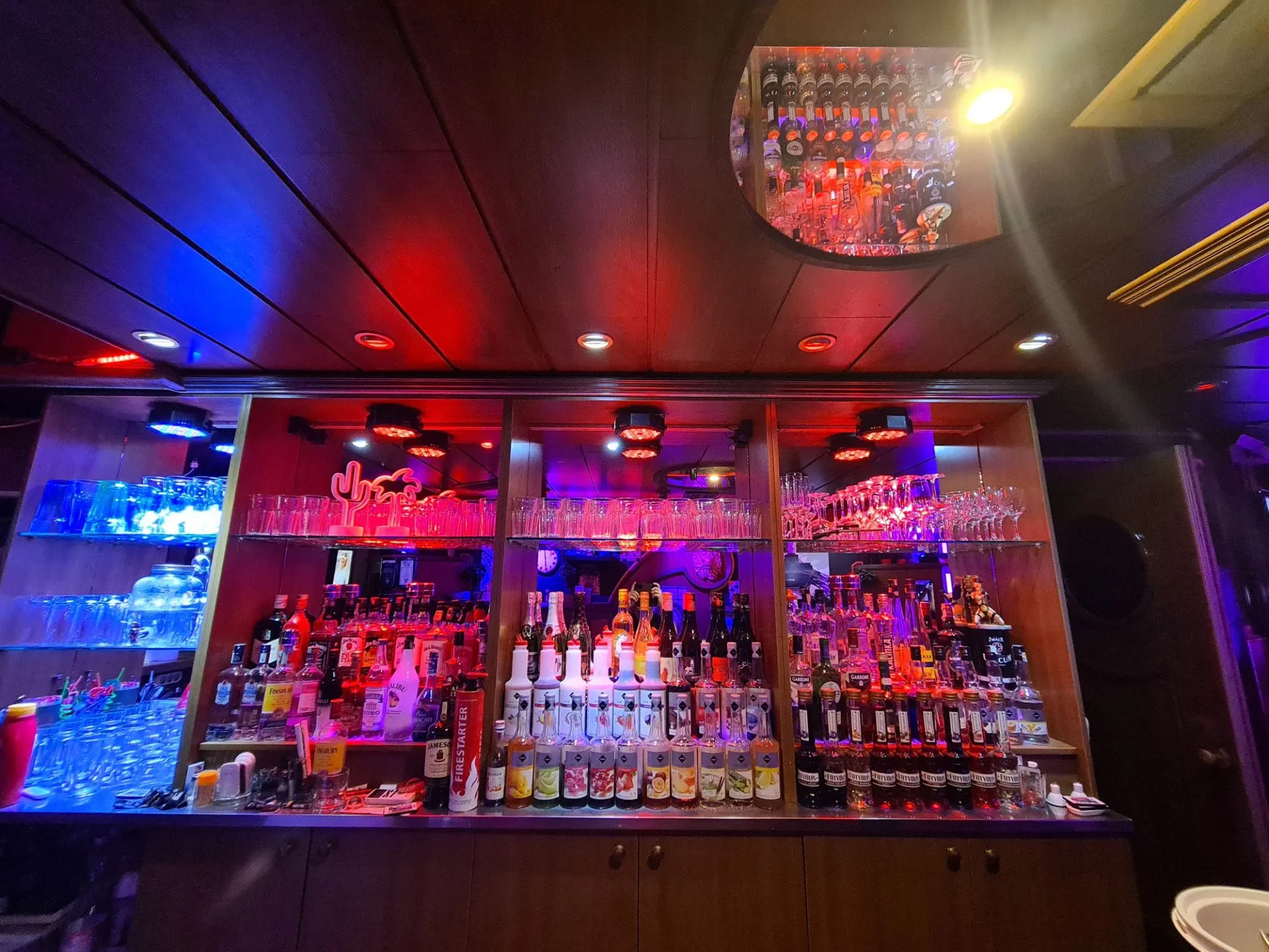 Back-bar shelves of bottles and glasses lit in blue and red