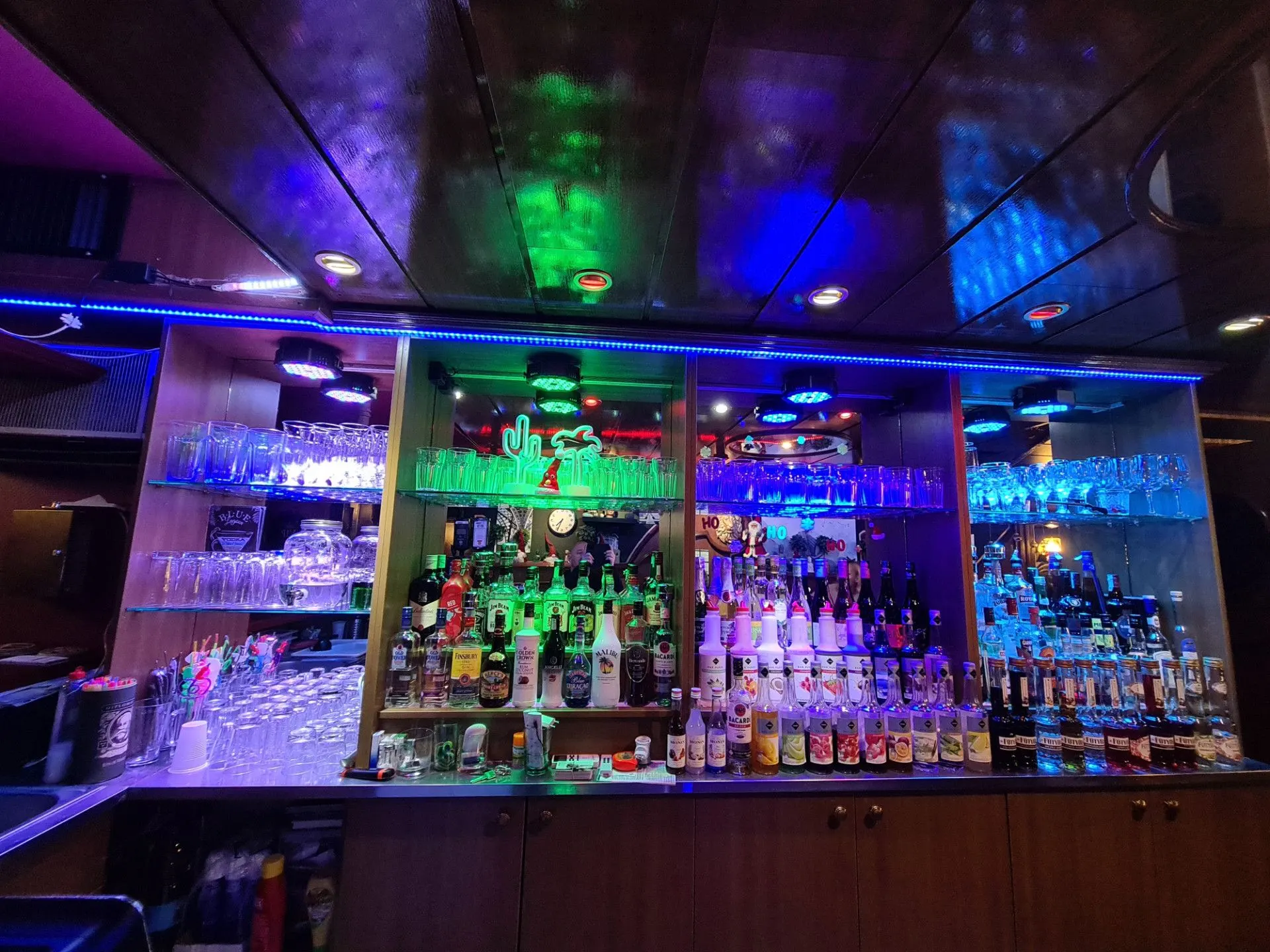 Back-bar shelves with bottles and glasses in blue-green light