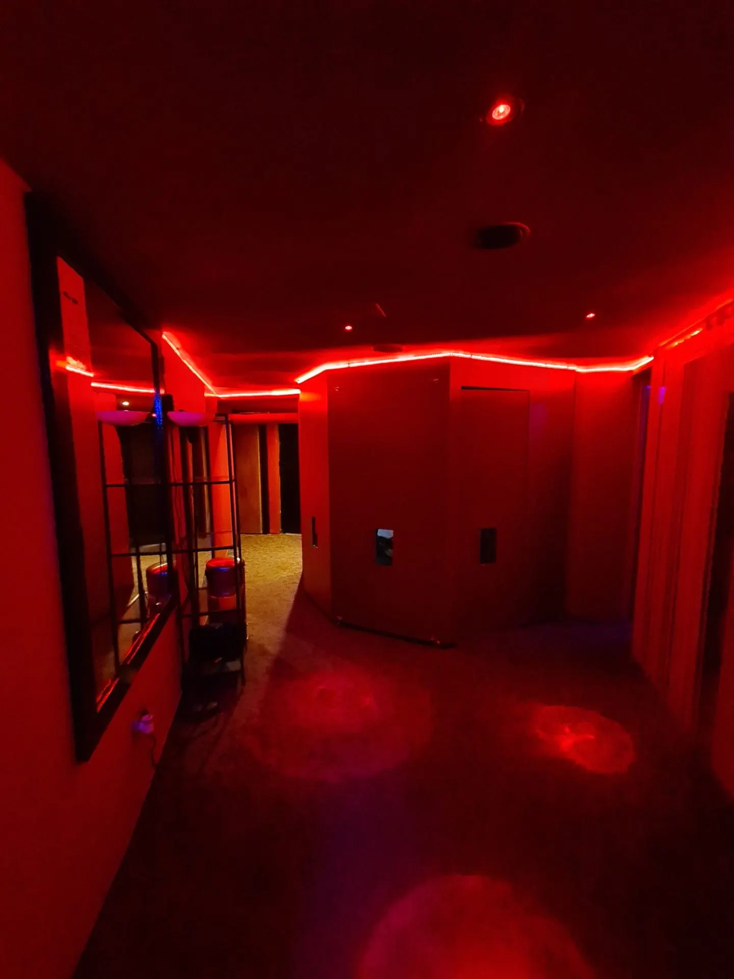 Corridor lit by a red light strip leading towards the rooms