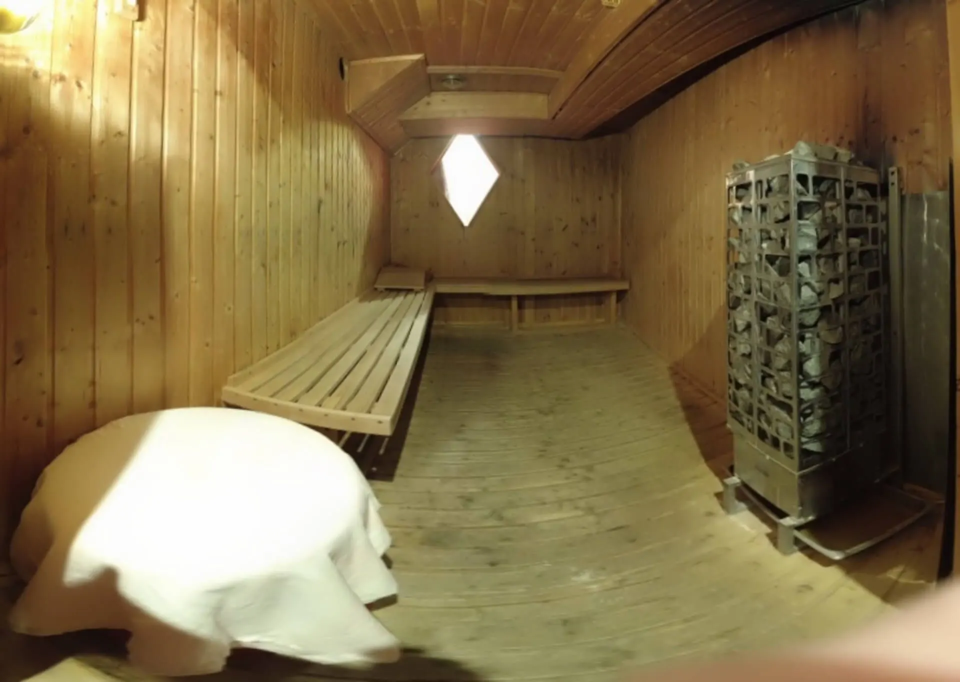 Wood-panelled sauna with a bench, stone heater and towel